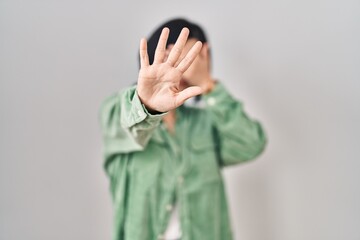 Sticker - Young asian woman standing over white background covering eyes with hands and doing stop gesture with sad and fear expression. embarrassed and negative concept.