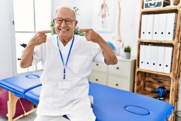 Canvas Print - Senior physiotherapy man working at pain recovery clinic smiling cheerful showing and pointing with fingers teeth and mouth. dental health concept.