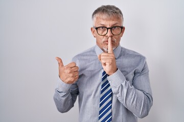 Sticker - Hispanic business man with grey hair wearing glasses asking to be quiet with finger on lips pointing with hand to the side. silence and secret concept.