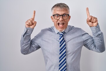 Canvas Print - Hispanic business man with grey hair wearing glasses smiling amazed and surprised and pointing up with fingers and raised arms.