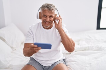 Sticker - Middle age grey-haired man listening to music sitting on bed at bedroom