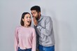 © Krakenimages.com - Young hispanic couple standing together hand on mouth telling secret rumor, whispering malicious talk conversation