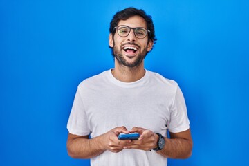 Canvas Print - Handsome latin man using smartphone typing message smiling and laughing hard out loud because funny crazy joke.