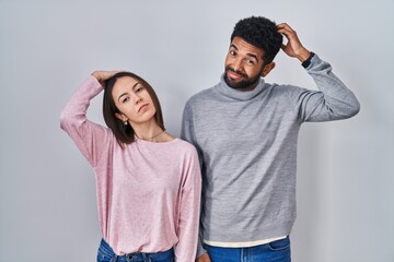 Wall Mural - Young hispanic couple standing together confuse and wondering about question. uncertain with doubt, thinking with hand on head. pensive concept.