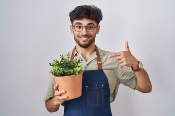 Sticker - Arab man with beard holding green plant pot looking confident with smile on face, pointing oneself with fingers proud and happy.