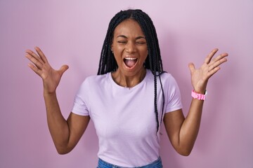 Poster - African american woman with braids standing over pink background celebrating mad and crazy for success with arms raised and closed eyes screaming excited. winner concept