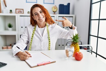 Poster - Young redhead woman nutritionist doctor at the clinic looking confident with smile on face, pointing oneself with fingers proud and happy.