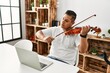© Krakenimages.com - Young hispanic man having online violin lesson using laptop sitting on the table at home.