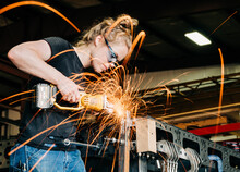 A Female Craftsman Cuts Metal And Sparks Fly