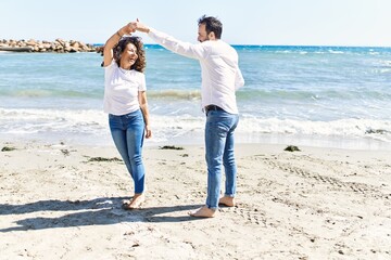 Sticker - Middle age hispanic couple smiling happy dancing at the beach.