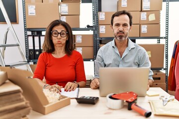 Poster - Middle age couple working at small business ecommerce puffing cheeks with funny face. mouth inflated with air, crazy expression.