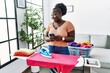 © Krakenimages.com - Young african american woman using smartphone ironing clothes at home