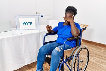 Sticker - Young african woman sitting on wheelchair voting putting envelop in ballot box covering eyes with hand, looking serious and sad. sightless, hiding and rejection concept