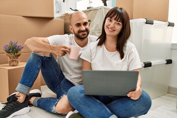 Sticker - Young hispanic couple smiling happy using laptop drinking coffee at new home.