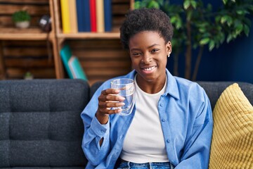 Poster - African american woman drinking glass of water looking positive and happy standing and smiling with a confident smile showing teeth