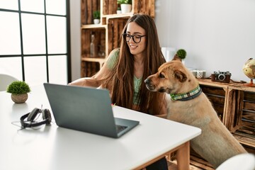 young hispanic woman using laptop sitting on table with dog at home