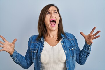 Sticker - Middle age brunette woman wearing casual denim jacket over isolated background crazy and mad shouting and yelling with aggressive expression and arms raised. frustration concept.