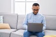 © Krakenimages.com - Young hispanic man using laptop and earphones sitting on sofa at home