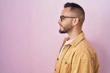 Poster - Young hispanic man standing over pink background looking to side, relax profile pose with natural face with confident smile.