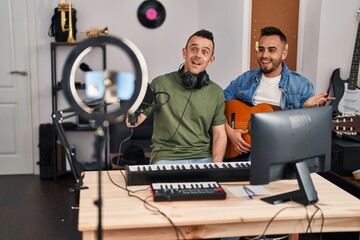 Canvas Print - Two men playing classic guitar at music studio recording song celebrating achievement with happy smile and winner expression with raised hand