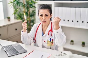 Canvas Print - Young doctor woman holding blood sample annoyed and frustrated shouting with anger, yelling crazy with anger and hand raised