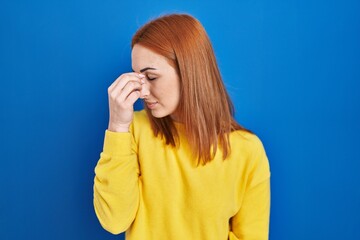 Poster - Young woman standing over blue background tired rubbing nose and eyes feeling fatigue and headache. stress and frustration concept.