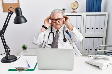 Poster - Senior caucasian man wearing doctor uniform and stethoscope at the clinic trying to hear both hands on ear gesture, curious for gossip. hearing problem, deaf