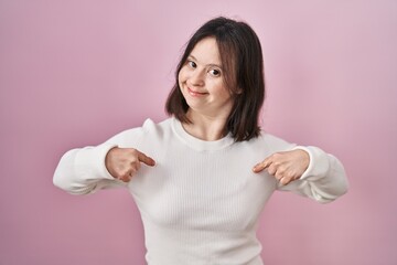 Wall Mural - Woman with down syndrome standing over pink background looking confident with smile on face, pointing oneself with fingers proud and happy.