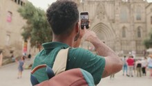 Young Man Tourist Takes Photo On Cellphone While Standing On The Square Of The Old City. Back View