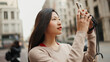 Beautiful Asian woman looking inspired taking photos of beautiful architecture using smartphone for it. Female Asian tourist exploring European city