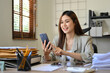 © bongkarn - Attractive Asian businesswoman at her office desk, using her smartphone to check her email.