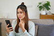 © bongkarn - Pretty Asian girl using smartphone while relaxing in her living room. reading online blog