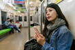 © PR Image Factory - asian Japanese girl traveler sitting on seat in train car and searching travel info on the phone while taking train to inari station in Kyoto japan.