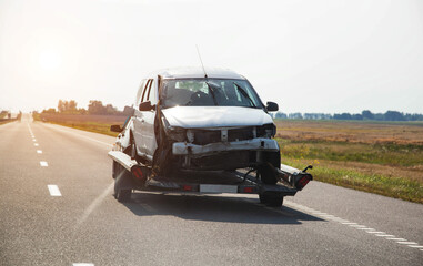 Transportation of a car broken in an accident on a light trailer. Road accident, wrecked car delivery campaign. Transportation of a car on a trailer on a motorway in summer. Copy space for text