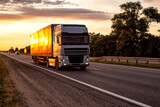 A semitrailer tractor with a tilt semitrailer transports cargo against the backdrop of an evening sunny sunset in summer. The concept of the logistics system and the business of cargo transportation