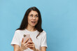 © Tatiana - a happy, joyful woman with beautiful long hair, in a light T-shirt, stands with a fashionable phone in her hands. Horizontal photo on a light blue background with space for text