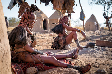 Wall Mural - Himba women sitting outside their huts in a traditional Himba village near Kamanjab, northern Namibia, Africa.