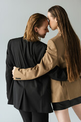 Wall Mural - back view of woman with long hair embracing young lesbian girlfriend isolated on grey.