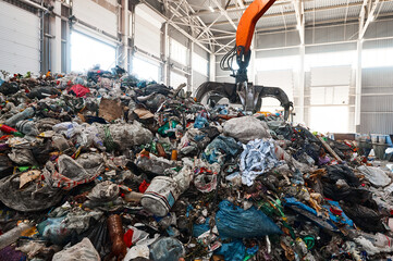 Excavator grabs trash in warehouse of waste processing plant