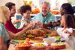 © Monkey Business - Multi-Generation Family Celebrating Thanksgiving At Home Eating Meal And Doing Cheers With Water