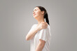 A young woman holds her shoulder with her hand, feeling pain. Gray background. The concept of health insurance and injuries of ligaments and joints