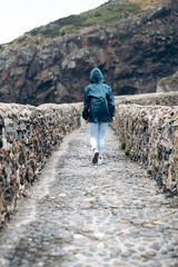 woman wearing a raincoat walking along a paved road enclosed by two stone walls