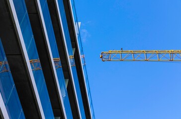 Canvas Print - Yellow crane mirrored in a modern glass building with blue sky