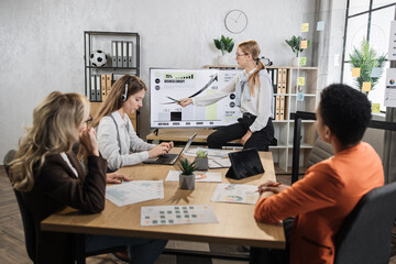 Wall Mural - Caucasian woman pointing on monitor with financial report during conference with multiracial female partners. Business woman colleagues gathering at office room for brainstorming.