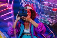 Young Woman Photographing Through Instant Camera In Front Of Shopping Cart