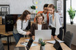 © sofiko14 - Group of confident high-skilled multiracial business women, standing at the table and discussing business strategy, while senior aged lady working on project on laptop computer.