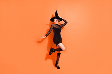 Wall Mural - Full size photo of cute young woman have fun nightclub party dressed trendy black halloween witch look isolated on orange color background