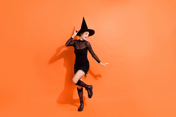 Wall Mural - Full body photo of charming young girl dancing costume party wear stylish black halloween witch garment isolated on orange color background