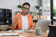 © sofiko14 - Portrait of attractive african business woman in headset sitting at office desk and looking at camera. Business lady having video conference showing thumb up. Business meeting online.
