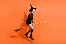 Full Size Photo Of Pretty Woman Flying Broom Sabbath Shopping Dressed Trendy Black Halloween Garment Isolated On Orange Color Background